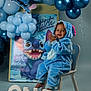 baby, child, blue_costume, stitch, birthday, balloons, chair, smiling, clapping, celebration, decorations, poster, happy, first_birthday, costume, indoor, person, footwearless, letters, event