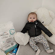 Eléna participe au concours pour gagner de l'argent avec cette photo : baby, infant, child, teddy_bear, plush_toy, leather_jacket, floral_pants, socks, heart_pillow, baby_wipes, diaper_pack, nursery_corner, wall, bedding, soft_toy, smile, portrait, sitting, cozy, cute