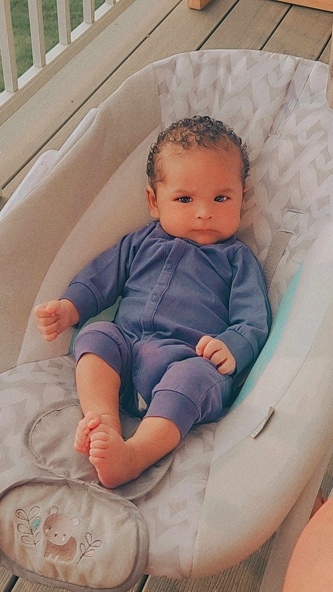 Ezmari joined the competition — help win amazing prizes! baby, infant, onesie, baby_seat, cushion, bear_patch, wooden_floor, porch, railing, curly_hair, barefoot, serious_expression, child, person, indoors, comfortable, cute, young_child, seated, portrait