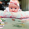 baby, infant, tummy_time, headband, pink_bow, blue_eyes, pillow, floral_pattern, blanket, cute, indoors, portrait, child, young_baby, soft_lighting, closeup, adorable, sleepwear, resting, baby_girl