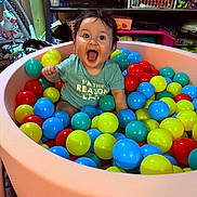 Nova is registered to the contest to win money with this photo: baby, child, ball_pit, colorful_balls, indoor, happy, smiling, sitting, toys, shelf, plastic_balls, play, cute, person, toddler, clothing, face, expression, mouth_open, hair