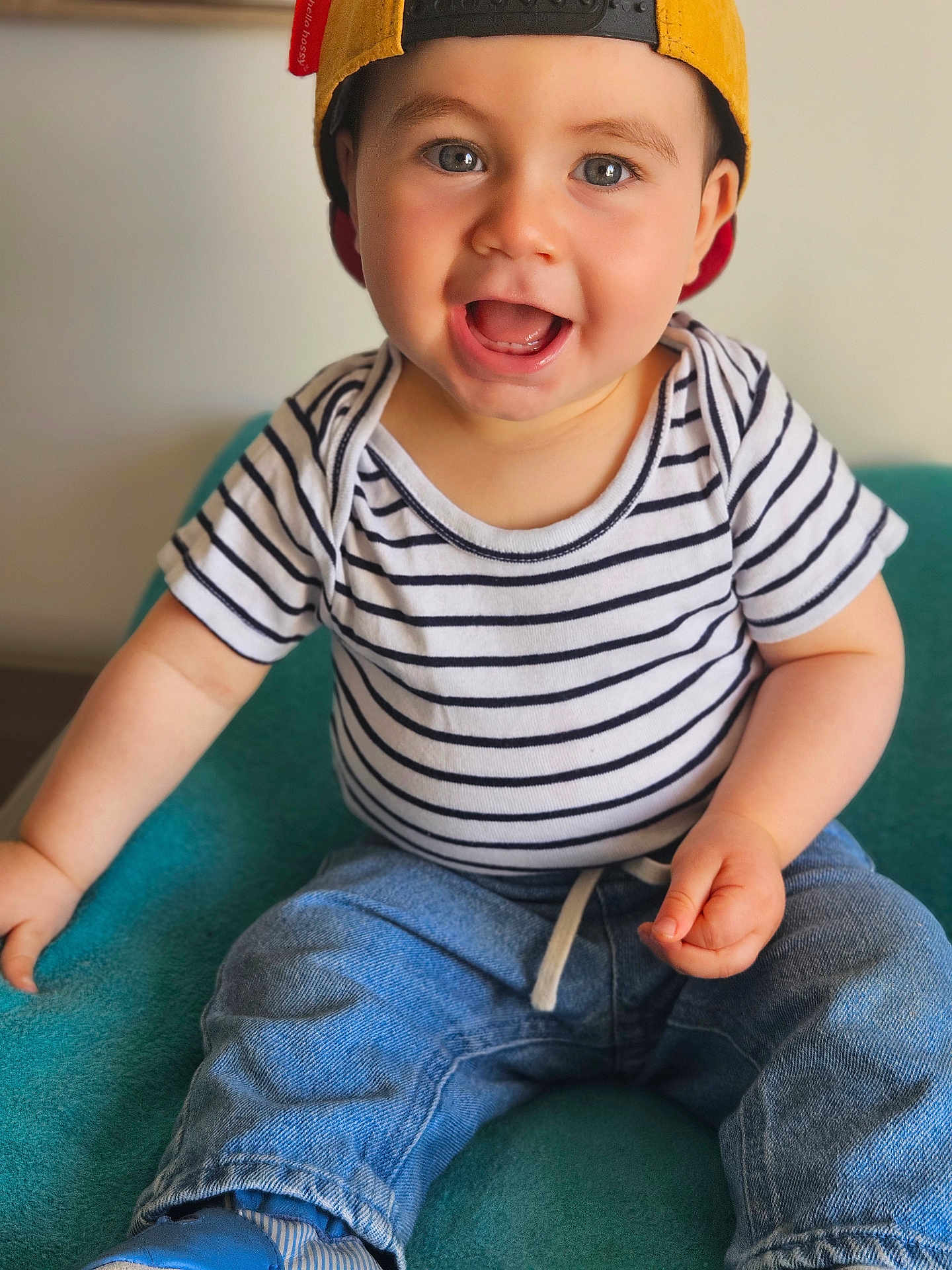 Charly a rejoint le concours — aidez-le/la à gagner de superbes lots ! toddler, child, smiling, cap, striped_shirt, jeans, blue_shoes, sitting, indoor, happy, person, face, headwear, casual_clothing, blue, white, teal_chair, cute, young_child, portrait
