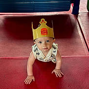 Bentley joined the competition — help win amazing prizes! baby, child, crawling, burger_king_crown, indoor, playground, red_floor, blue_eyes, curious, cute, infant, paper_crown, clothing, plastic_play_structure, hands, face, looking_up, floor_mat, toddler, person