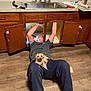 cabinet, casual_clothing, curtain, dog, floor, glasses, home_interior, indoor, kitchen, man, pet, pipe, plumbing, relaxed, repair, sink, small_dog, window, wood_floor, working