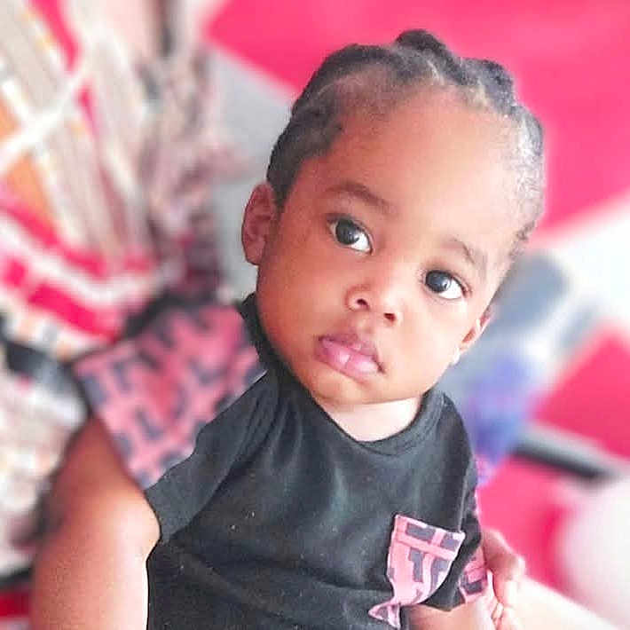 Happy a rejoint le concours — aidez-le/la à gagner de superbes lots ! black_shirt, braided_hair, casual_clothing, child, colorful_background, curious, cute, expression, face, human, indoor, looking, person, pink_pocket, portrait, seated, skin, small_person, toddler, young_child