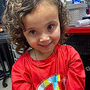 Brooklynn joined the competition — help win amazing prizes! child, curly_hair, smile, red_shirt, necklace, heart_shaped_jewelry, peace_symbol, indoor, countertop, bottles, casual, portrait, happy, person, face, young, cute, candid, colorful, jewelry