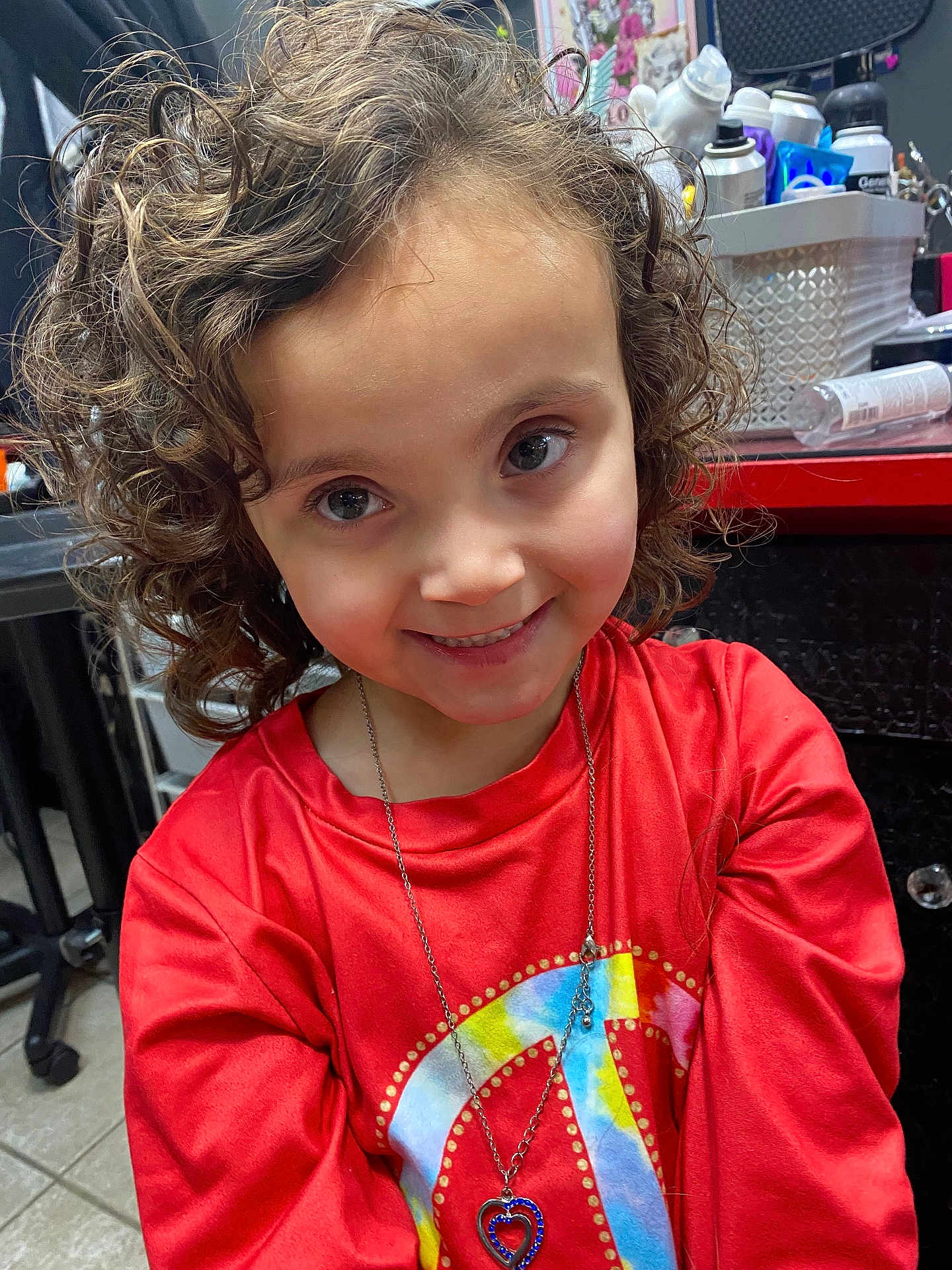 Brooklynn joined the competition — help win amazing prizes! child, curly_hair, smile, red_shirt, necklace, heart_shaped_jewelry, peace_symbol, indoor, countertop, bottles, casual, portrait, happy, person, face, young, cute, candid, colorful, jewelry
