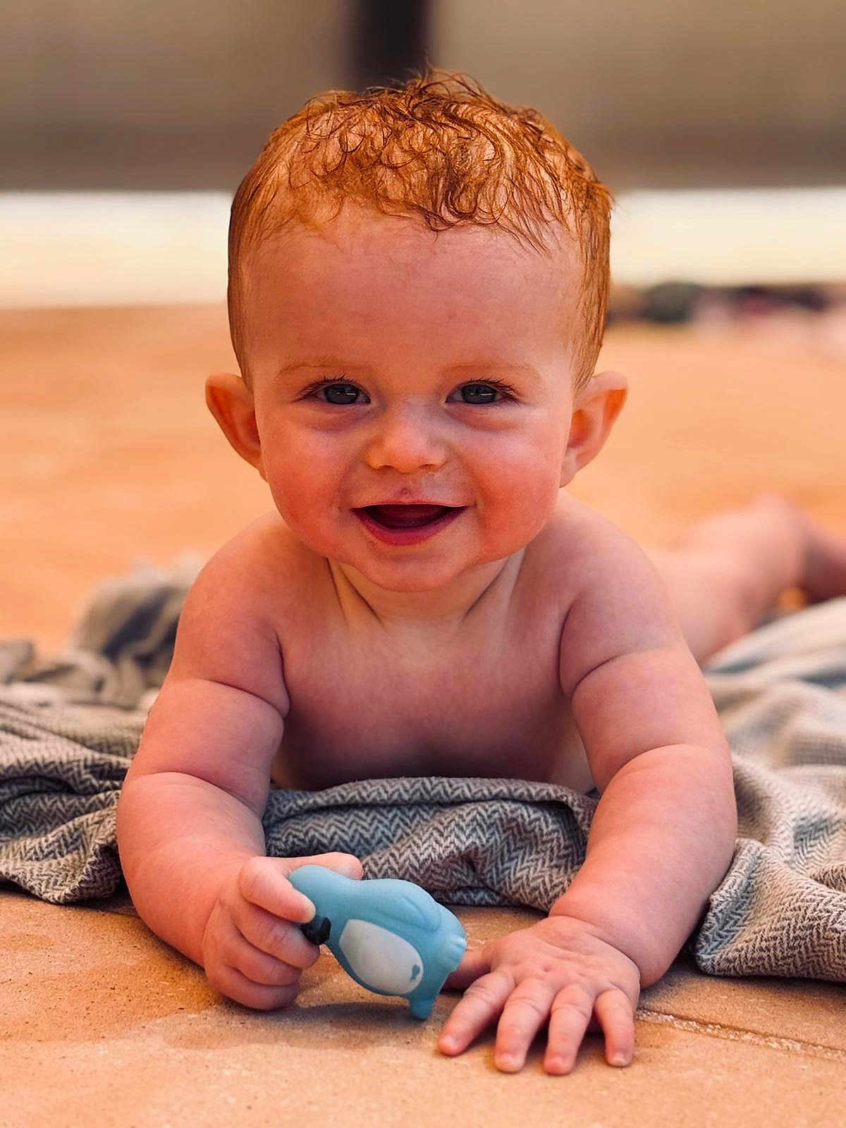 Noé participe au concours pour gagner de l'argent avec cette photo : baby, child, smiling, toy, blue_toy, penguin_toy, blanket, curly_hair, skin, face, hands, tummy, indoor, floor, closeup, happy, cute, infant, portrait, playful