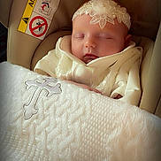 Charlize joined the competition — help win amazing prizes! baby, sleeping, infant, white_clothing, headband, flower, blanket, cross, car_seat, airbag_warning, peaceful, closeup, indoors, soft_lighting, cute, portrait, child, newborn, resting, adorable
