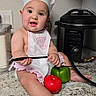 baby, child, chef_hat, apron, kitchen, countertop, knife, green_bell_pepper, tomato, pressure_cooker, cooking, cute, infant, playing, food, person, indoor, curious, sitting, smiling