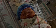 Ryder joined the competition — help win amazing prizes! newborn, baby, hospital, bassinet, blanket, footprint_pattern, blue_hat, sleeping, infant, swaddled, crib, medical, name_card, person, resting, indoors, soft_lighting, peaceful, cute, child