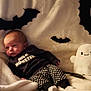 baby, bat_decorations, black_and_white, blanket, child, clothing, costume, cozy, cute, decor, ghost_plush, halloween, holiday, indoors, infant, patterned_pants, plush_toy, resting, smiling_toy, soft_texture