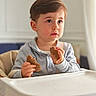 Joud Rayan participe au concours pour gagner de l'argent avec cette photo : toddler, child, high_chair, bread, food, indoor, portrait, curious, baby, eating, person, young_child, seated, casual_clothing, light, home, cute, face, hands, expression