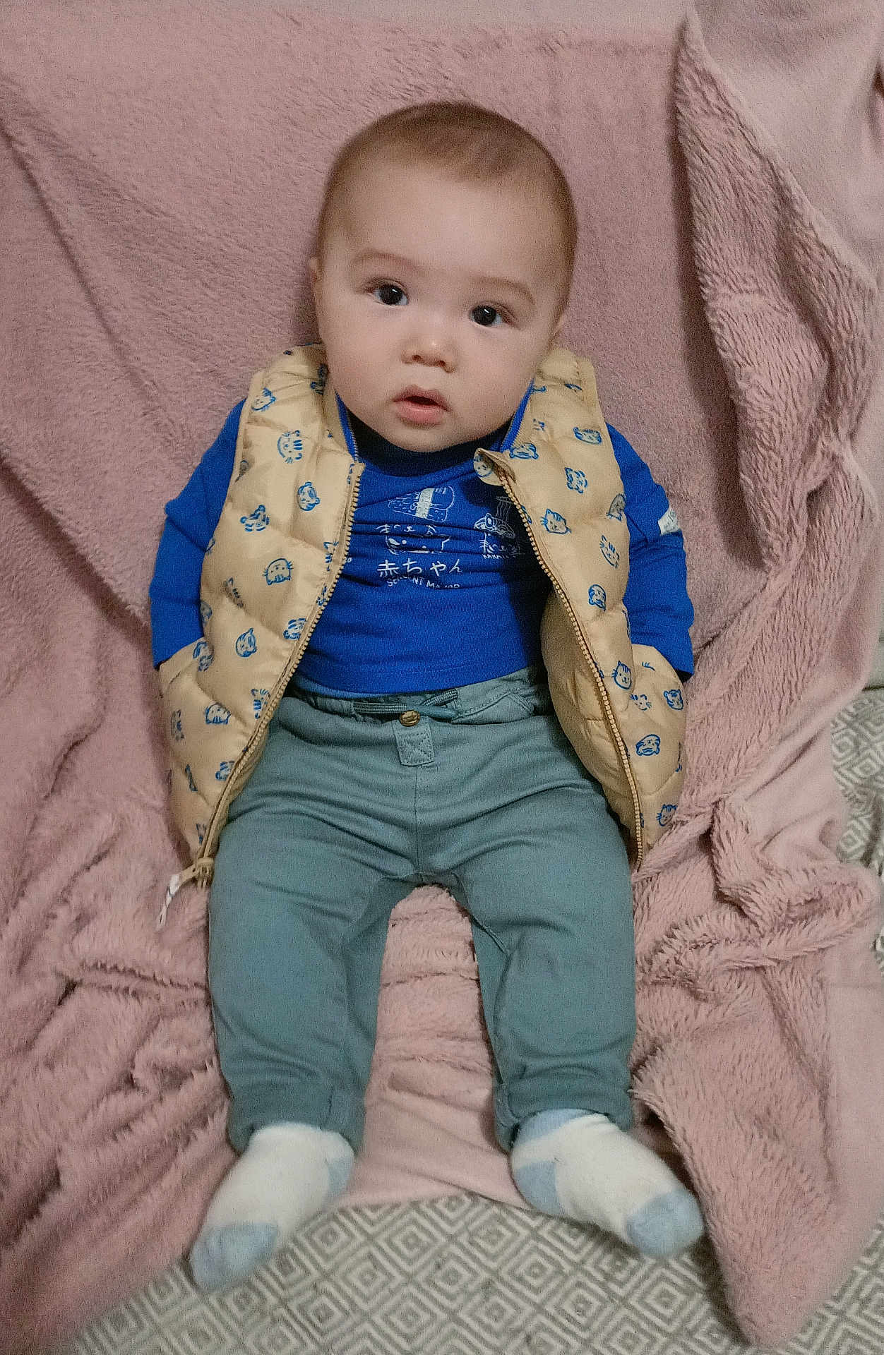 Lilio participe au concours pour gagner de l'argent avec cette photo : baby, child, infant, vest, blue_shirt, gray_pants, socks, blanket, soft_texture, indoor, seated, curious_expression, face, head, person, clothing, cute, young_child, portrait, floor_mat