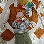 baby, infant, toy, playmat, plush_toy, teething_ring, striped_shirt, green_pants, hand, giraffe_toy, soft_toy, floor_mat, child, cute, indoor, playtime, colorful, person, lying_down, curious