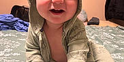 Jimmy is registered to the contest to win money with this photo: baby, child, smiling, hooded_clothing, bed, blanket, hand, foot, indoors, portrait, cute, person, infant, happy, skin, clothing, sitting, room, cozy, casual