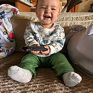 Jimmy joined the competition — help win amazing prizes! baby, carpet, child, couch, cozy, cushions, cute, dinosaur_pattern, green_pants, happy, home, indoor, living_room, person, remote_control, sitting, smiling, socks, sweater, toy