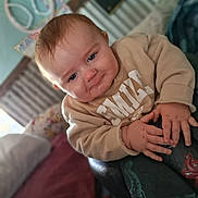 Dustin is registered to the contest to win money with this photo: baby, child, smile, face, hands, clothing, sweatshirt, pants, dinosaur, indoor, bed, pillow, blanket, furniture, person, portrait, cute, infant, expression, home
