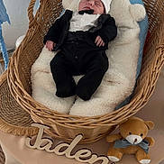 Jaden a rejoint le concours — aidez-le/la à gagner de superbes lots ! baby, tuxedo, sleeping, wicker_basket, balloons, blue, soft_padding, teddy_bear, bow, wooden_letters, name_sign, table, blanket, infant, cute, cozy, newborn, portrait, indoor, celebration