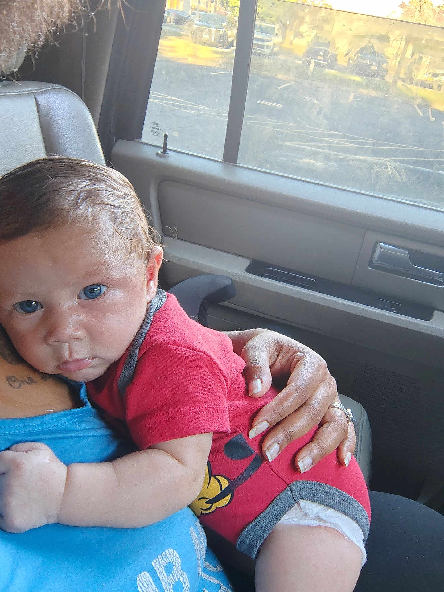 Sebastian joined the competition — help win amazing prizes! baby, child, infant, blue_eyes, red_onesie, cartoon_print, adult_hand, car_interior, window, seat, tattoo, skin, comfort, resting, close_up, portrait, natural_light, caring, family, tender_moment