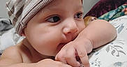 Emiliano joined the competition — help win amazing prizes! baby, infant, hat, striped_hat, chewing, arm, closeup, face, skin, hand, fingers, bed, blanket, pattern, comfort, indoors, child, cute, expression, resting