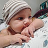 baby, infant, hat, striped_hat, chewing, arm, closeup, face, skin, hand, fingers, bed, blanket, pattern, comfort, indoors, child, cute, expression, resting