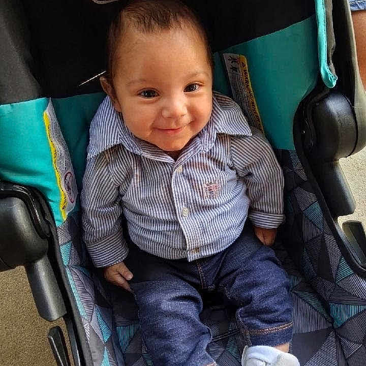 Emiliano joined the competition — help win amazing prizes! baby, child, smiling, stroller, striped_shirt, blue_pants, white_shoes, infant, cute, seated, happy, indoors, clothing, footwear, person, portrait, baby_girl, baby_boy, casual, seat