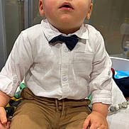 Axel a rejoint le concours — aidez-le/la à gagner de superbes lots ! toddler, child, boy, white_shirt, bow_tie, brown_pants, sitting, indoor, curious_expression, hand, face, portrait, clothing, fashion, cute, young_child, casual, baby, home, person