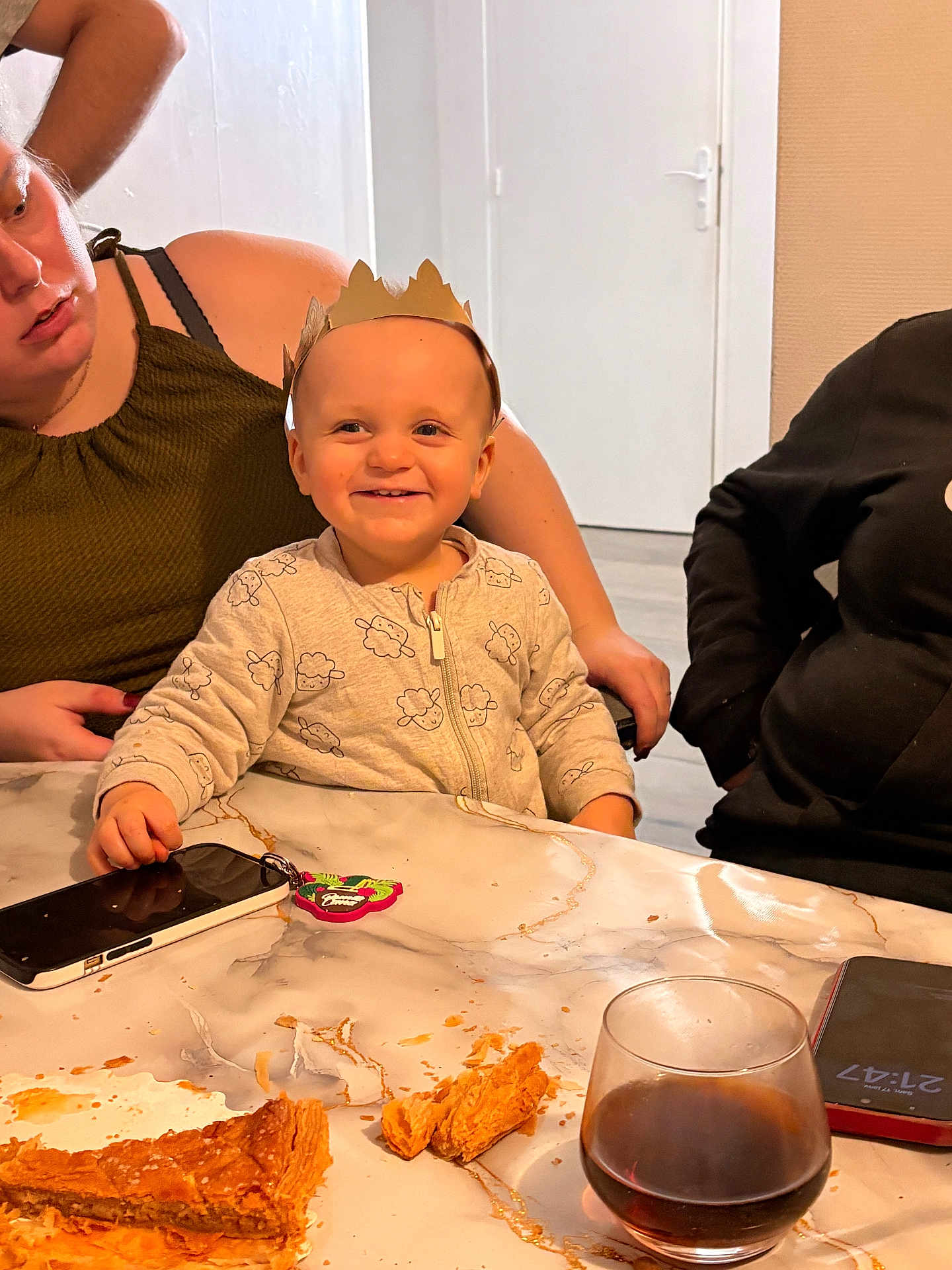 Axel a rejoint le concours — aidez-le/la à gagner de superbes lots ! toddler, child, smile, crown, table, pastry, crumbs, glass, beverage, adult, woman, indoor, family, happy, clothing, phone, keychain, marble_table, person, casual