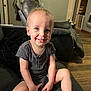 toddler, child, smiling, blue_eyes, sitting, couch, gray_clothing, barefoot, living_room, wooden_floor, recliner, indoor, person, happy, short_hair, home, casual, furniture, playful, cute