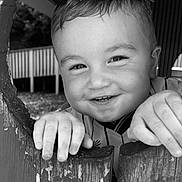 Kylo is registered to the contest to win money with this photo: child, toddler, smiling, black_and_white, portrait, face, hands, wooden_fence, outdoor, playful, cute, happy, close_up, peeking, expression, young, casual_clothing, texture, rustic, daylight