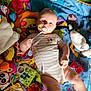 baby, pacifier, play_mat, toy, colorful, infant, child, lying_down, clothing, cute, soft_toy, patterned_mat, hand, leg, face, light, indoor, childhood, smiling, white_onesie
