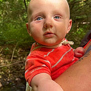 Maé a rejoint le concours — aidez-le/la à gagner de superbes lots ! baby, child, blue_eyes, red_shirt, striped_clothing, outdoor, forest, greenery, nature, person, holding, arm, tattoo, daylight, stream, curious, infant, portrait, closeup, human