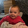 Chippy is registered to the contest to win money with this photo: baby, child, smiling, blanket, pink_clothing, indoor, face, cute, cozy, furniture, dresser, brick_wall, portrait, happy, toddler, young_child, warm, home, person, soft_texture