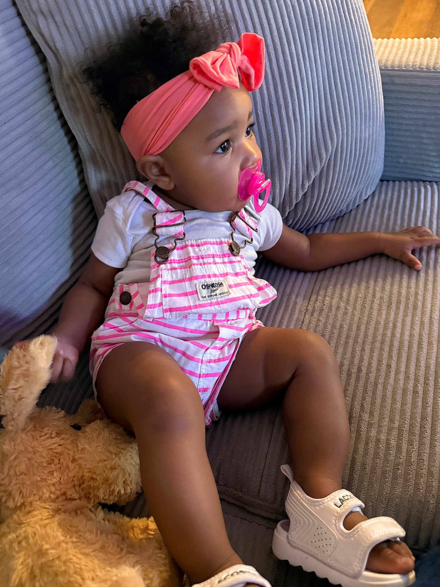 Talaija joined the competition — help win amazing prizes! baby, child, couch, curly_hair, cute, gray_couch, headband, indoor, overalls, pacifier, pink_headband, plush_toy, relaxed, seated, side_view, soft_lighting, striped_clothing, teddy_bear, toddler, white_sandals
