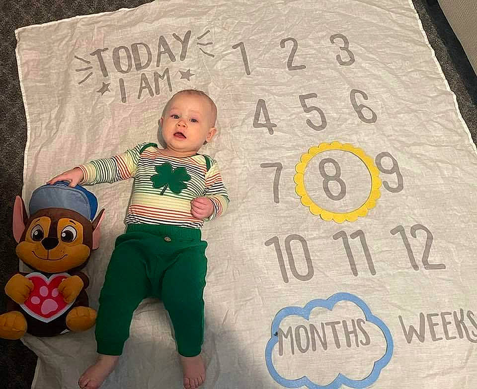 Erikson is registered to the contest to win money with this photo: baby, baby_toddler_clothing, bedding, child, cool, facial_expression, fictional_character, flooring, font, happy, illustration, linens, pajamas, pattern, person, photo_caption, room, sleeve, t_shirt, toddler
