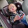 child, toddler, car_seat, vehicle_interior, red_hair, puckered_lips, seatbelt, plaid_shirt, blue_jeans, cup, toy, window, tree_outside, car_door, car_seat_harness, child_safety, funny_face, indoor, person, seat