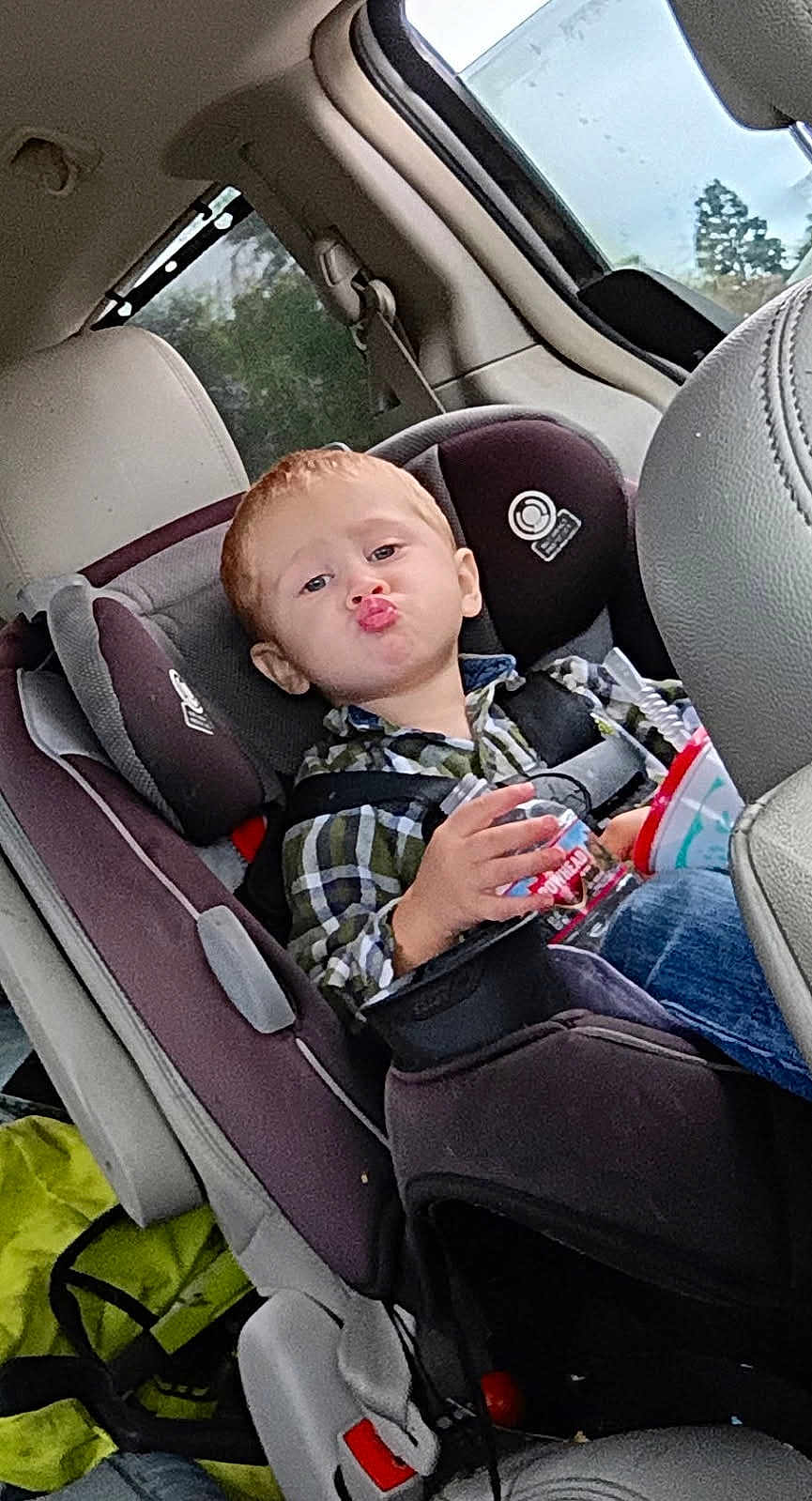 Dantyvious is registered to the contest to win money with this photo: child, toddler, car_seat, vehicle_interior, red_hair, puckered_lips, seatbelt, plaid_shirt, blue_jeans, cup, toy, window, tree_outside, car_door, car_seat_harness, child_safety, funny_face, indoor, person, seat