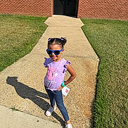 Emma joined the competition — help win amazing prizes! brick_wall, casual_clothing, child, girl, grass, hair_buns, happy, jeans, necklace, outdoor, person, pose, purple_shirt, shadow, sidewalk, smile, sneakers, sunglasses, sunny, wristband