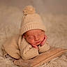 newborn, baby, sleeping, portrait, knitwear, hat, pom_pom, blanket, pillow, cream, cozy, indoors, infant, peaceful, resting, closeup, soft_lighting, textile, cuddly, photography