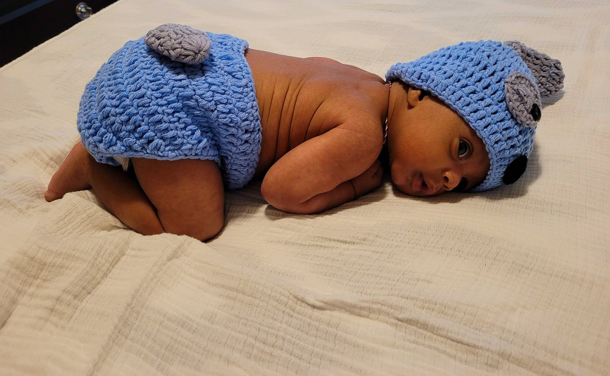 Mark is registered to the contest to win money with this photo: baby, cap, child, comfort, elbow, flooring, fun, hat, headgear, headwear, human_leg, knit_cap, landscape, linens, pattern, person, room, sand, toddler, toy