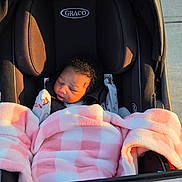 Niriyah Christina is registered to the contest to win money with this photo: baby, infant, child, stroller, blanket, pink_blanket, plaid, sleeping, face, portrait, outdoor, sunlight, sidewalk, walkway, car_seat, harness, newborn, cozy, black_stroller, street