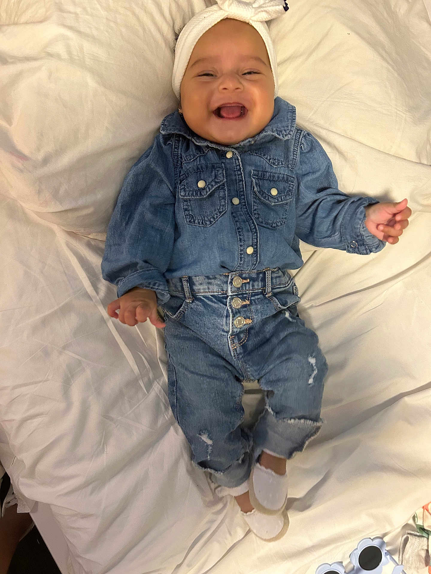 Keylee is registered to the contest to win money with this photo: baby, child, denim, jeans, shirt, headband, smiling, happy, infant, clothing, white_bed, footwear, shoes, baby_girl, portrait, cute, indoor, person, toddler, fashion