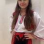 child, traditional_clothing, hat, apron, red, white, black, long_hair, smiling, portrait, indoor, wall, painting, hands_on_hips, costume, cultural, young, person, fashion, standing