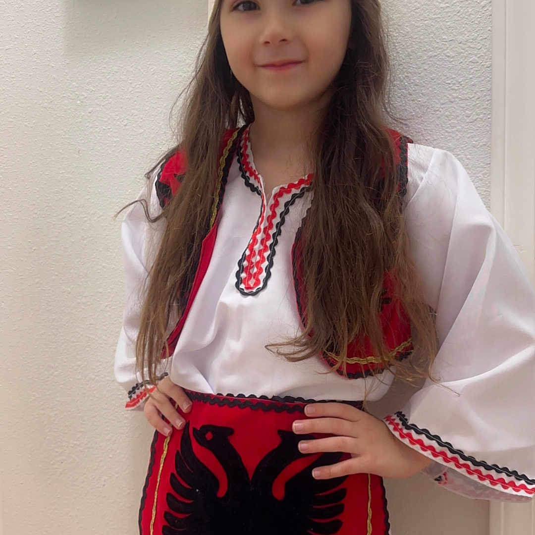 Klea joined the competition — help win amazing prizes! apron, black, child, costume, cultural, fashion, hands_on_hips, hat, indoor, long_hair, painting, person, portrait, red, smiling, standing, traditional_clothing, wall, white, young