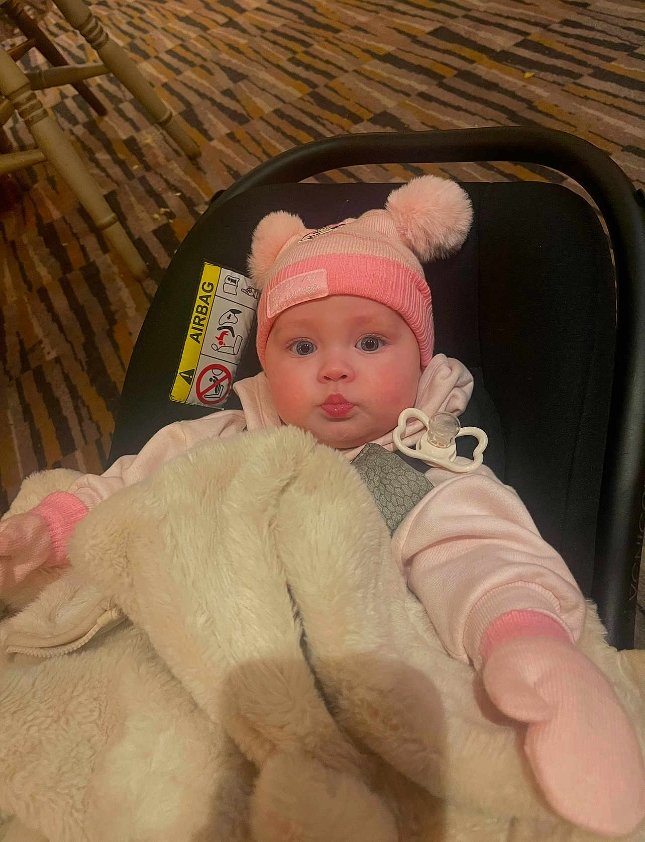 Laylah joined the competition — help win amazing prizes! baby, child, beanie, pink, mittens, blanket, car_seat, pacifier, face, indoor, cute, warm_clothing, expression, person, soft_texture, cozy, infant, headwear, seated, portrait