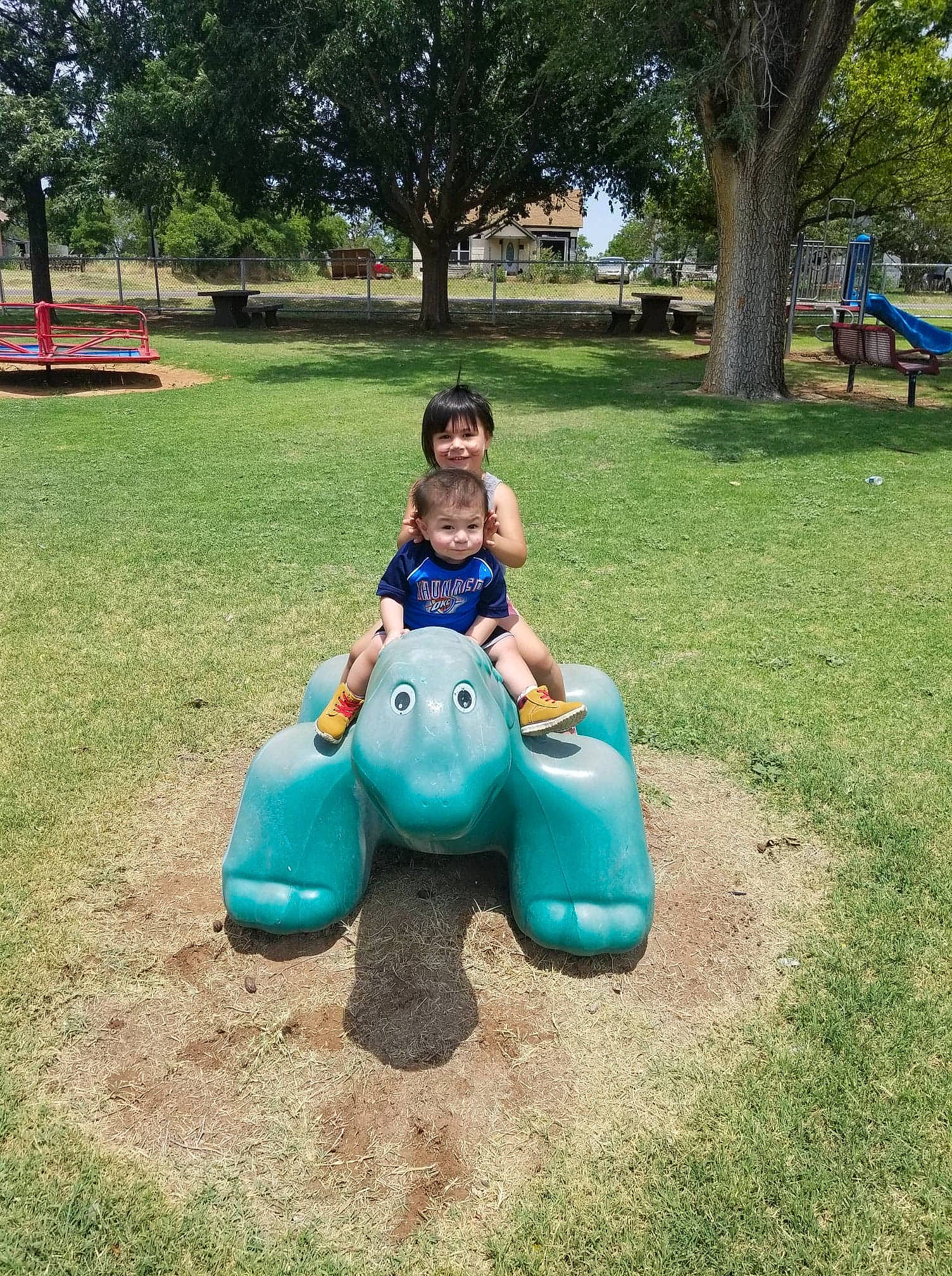 Marcus Jr. is registered to the contest to win money with this photo: aqua, baby_toddler_clothing, city, fun, grass, human_settlement, joy, lawn, leisure, outdoor_play_equipment, outdoor_recreation, park, person, play, playground, public_space, recreation, shade, sitting, summer