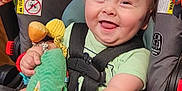 Finnegan is registered to the contest to win money with this photo: baby, car_seat, child, child_safety, clothing, corn_cob_toy, cute, fabric, feet, hands, happy, holding, indoor, infant, playful, red_bracelet, seatbelt, smiling, stuffed_animal, toy