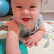 Finnegan is registered to the contest to win money with this photo: baby, smiling, crawling, child, play_mat, hand, face, indoor, floor, exercise_ball, happy, person, infant, skin, furniture, home, curly_hair, closeup, cute, young_child