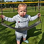 toddler, child, swing, playground, outdoor, grass, clothing, hoodie, shorts, socks, daylight, sky, clouds, fence, chain, shadow, person, expression, park, recreation
